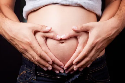 Hände formen ein Herz auf einem Schwangerschaftsbauch